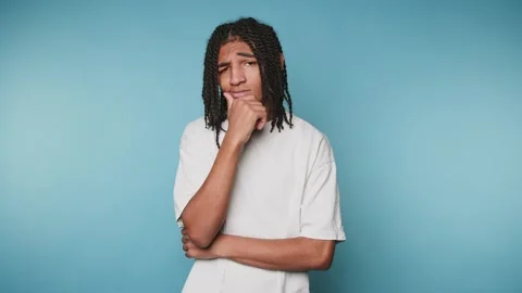 Young man poses with deep thought in front of a blue background in a studio.. Видео 328248767