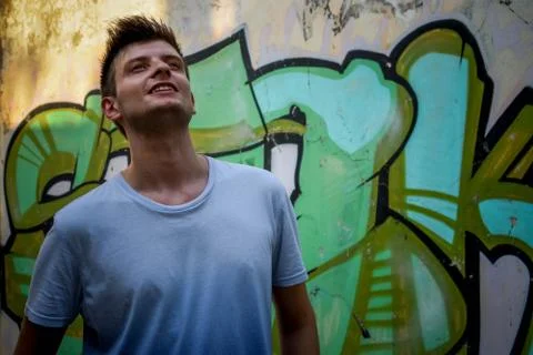 Young man posing beside a rustic wall painted with graffiti Stock Photos