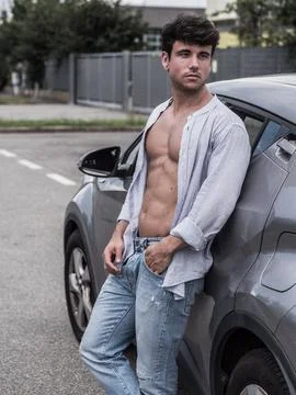 Young man posing confidently beside a parked car in urban area Stock Photos