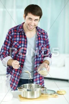 Young man pouring oat into saucepan to cook porridge Stock Photos
