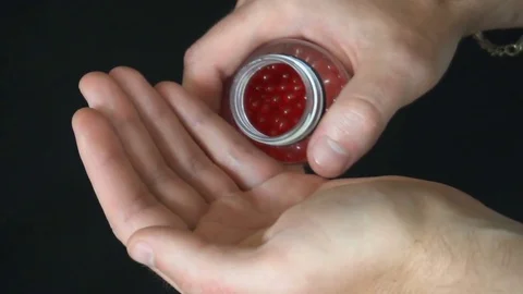 A young man pours it on the palm of his little red round pellets for strike ball Stock Footage 77082937