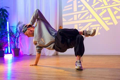 A young man practices a breakdancing move in a studio with colorful lighting Stockfoto's
