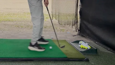 A young man practices his swing and hits a ball at an outdoor driving range.  Video stock 344556721
