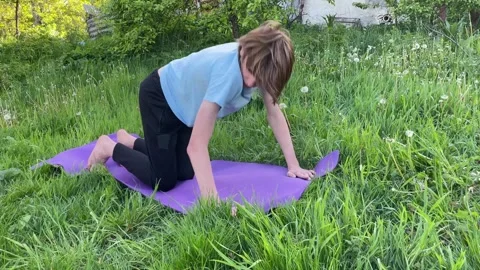 Young man practicing the cat cow yoga pose on a mat in a grassy backyard Stock Footage 283909392