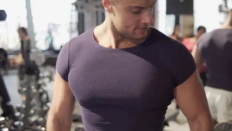 A young man is practicing at the gym. He pumps his arm muscles with dumbbells Stock Footage 73779447