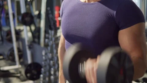 A young man is practicing at the gym. He pumps his arm muscles with dumbbells Stock Footage 73779619