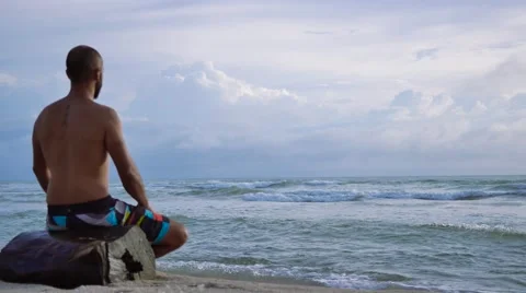Young man practicing meditation  on the beach at sunset time Stock Footage 67490705