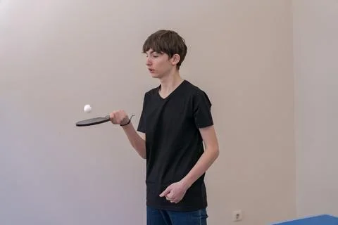 Young man practicing table tennis indoors, tossing ball with paddle Stock Photos