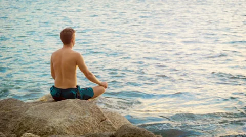 Young man practicing yoga. sits in a lotus position on the ocean shore Stock Footage 35423222