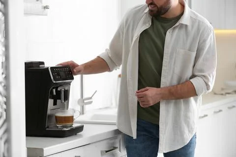 Young man preparing fresh aromatic coffee with modern machine in kitchen, clo Stock Photos