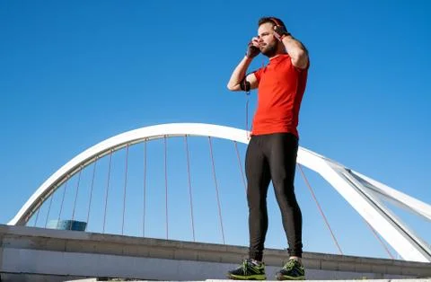 Young man preparing to run with a pair of headphones in front of a bridge Stock Photos