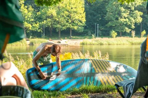 Young man preparing sup board for riding on shore of river Stock Photos