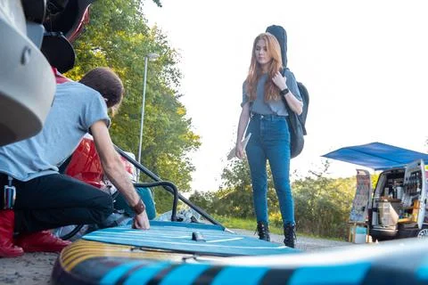 Young man preparing sup board for riding while his girlfriend standing near Stock Photos