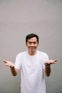 Young man presenting with open hands against neutral gray textured wall Stock Photos