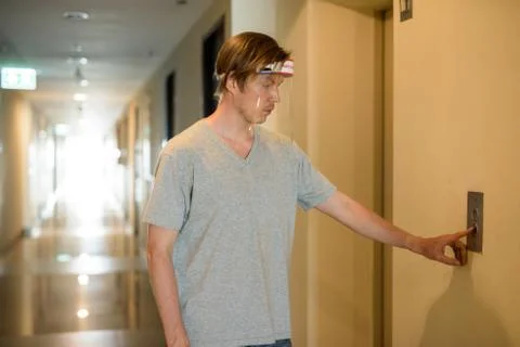 Young man pressing button of elevator with face shield for protection from Stockfoto's