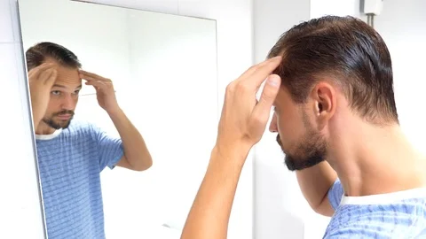 A young man with the problem of hair loss, looking in the mirror indoors Stock Footage 103518223
