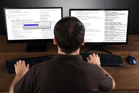 Young Man Programming Code On Computers Screen At Desk Foto stock