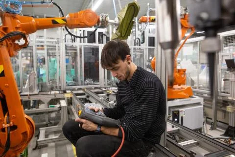Young man programming industrial automatic robot in automotive industry Stock Photos