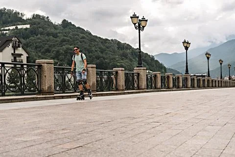 Young man in protective equipment riding on roller skates along embankment Stock Photos
