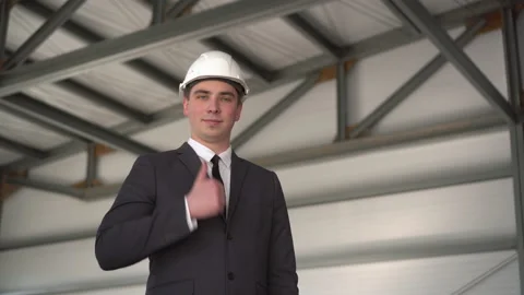 A young man in a protective helmet, shows a thumb at a construction site. The Stock Footage 134330601
