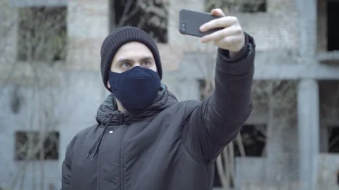 A young man in a protective mask sreams video with his smartphone against the Stock Footage 128331219