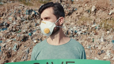 Young man in protective mask staying in toxic dirty place with tons of garbage Stock Footage 113819615