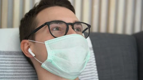 Young man in protective turquoise face mask relax, listens to music. Flu season. Stock-Footage 131476406