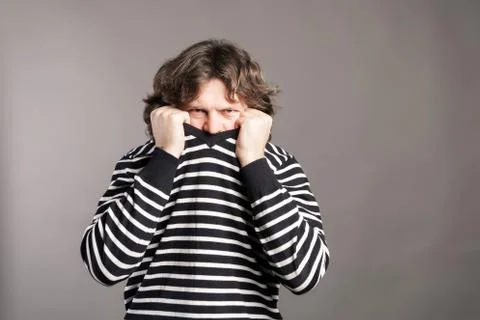 Young man pulling black and white striped sweater over head against gray back Stock Photos