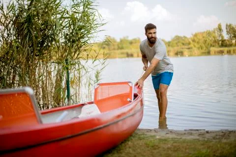 Young man pulling canoe into calm lake Stock Photos