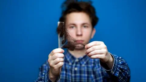 Young man pulling clusters of hair from a comb as a result of hair loss Stock Photos