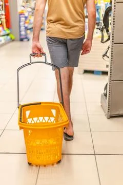 Young man pulling empty shopping basket through supermarket aisle Stock Photos