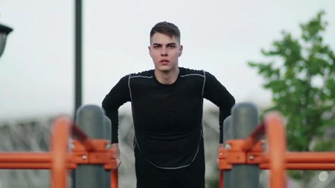 Young man is pulling up on horizontal bar while training in city park. Video stock 143502254