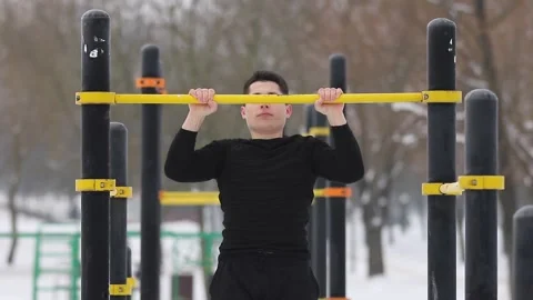 Young man pulls himself up on a horizontal bar on the street in winter. Video stock 154437247