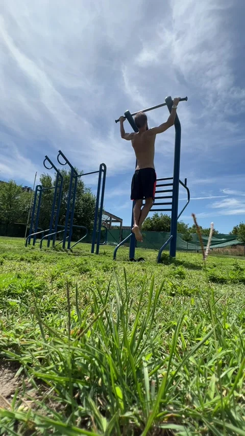 A young man pulls himself up on a horizontal bar on an open-air sports ground Stock Footage 247625349