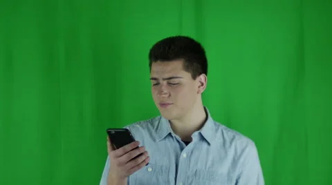 Young man pulls out phone and shrugs in front of a greenscreen Vidéo 59086254