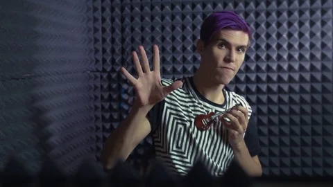 Young man with purple bangs playing on very little guitar in sound studio Stock Footage 70792160