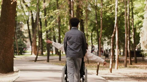 Young man pushing disabled girlfriend in wheelchair in park Stock Footage 294054376
