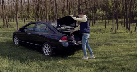 A young man puts the bag in the trunk and sits on the edge of the trunk. Stock Footage 130263758