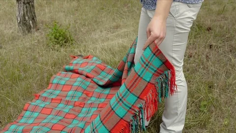 A young man puts a blanket on the grass in the park for a romantic dinner with a Stock Footage 77024965