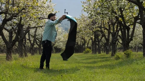 A young man puts a blanket on the grass in the park for a romantic dinner with a Stock Footage 90878697