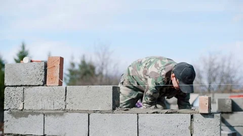 A young man puts the block on a solution. The builder builds a wall Stock Footage 79784989