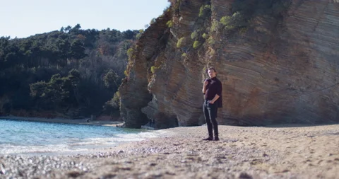 Young man puts coat over shoulder standing on sea beach Stock Footage 236594566