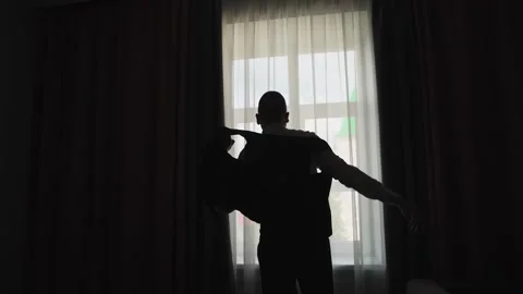 A young man puts on a jacket by the window Vídeos de archivo 327984762