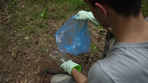 A young man puts a plastic bottle in a trash bag. Garbage collection Stock Footage 132136982
