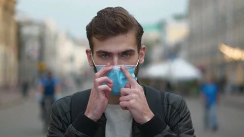 Young man puts on protective mask, he stands on busy street and look at you Video stock 143425353