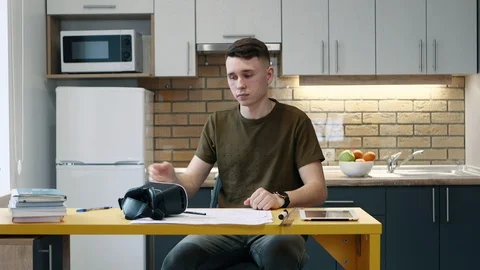 Young man puts on virtual reality glasses and works sitting on the kitchen at Stock Footage 103857824