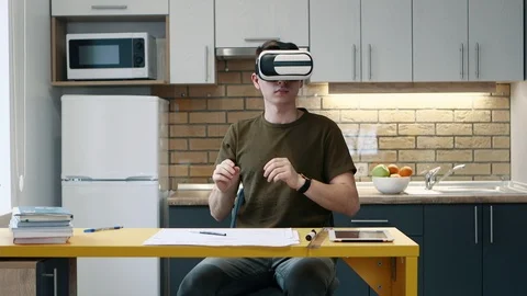 Young man puts on virtual reality glasses and works sitting on the kitchen at Stock-Footage 104429516