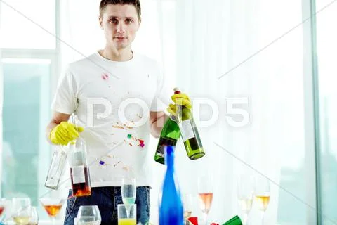 Young man putting away empty wine bottles after party Stock Photos