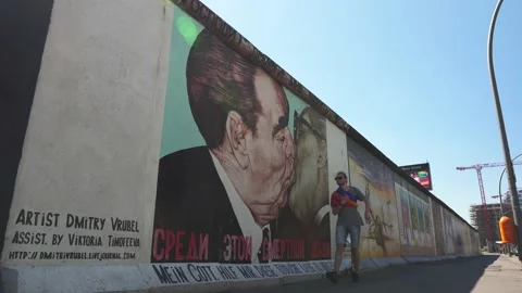 Young man with rainbow pride flag shawl walking by Berlin Wall, Eastside Gallery Stock Footage 159664177
