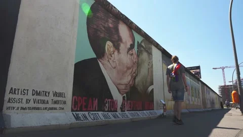 Young man with rainbow pride flag shawl walking by Berlin Wall, Eastside Gallery Stock Footage 159664266